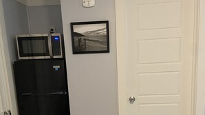 Una cocina compacta con un refrigerador negro, un microondas y un cuadro en la pared.