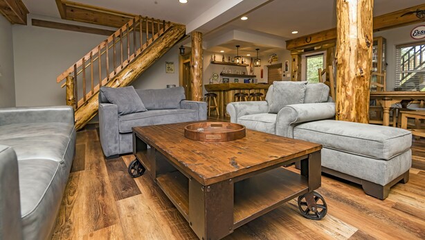 Ein geräumiges Wohnzimmer mit einer Holztreppe, grauen Sofas, einem Holztisch und einer Küchenzeile im Hintergrund.