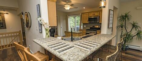 A spacious kitchen with a large island, wooden chairs, and a ceiling fan.