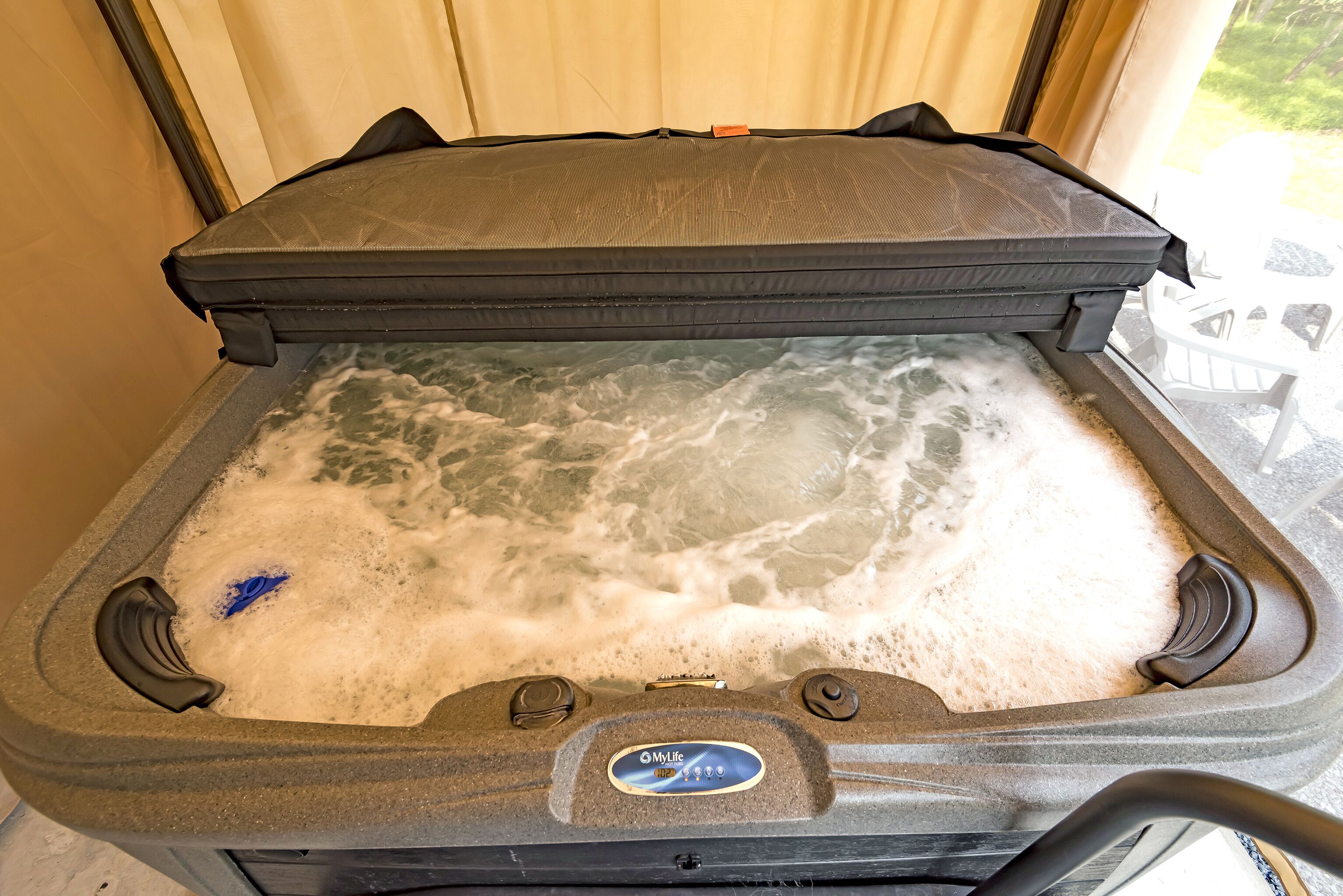 A hot tub with a cover, a control panel, and a view of the outdoors.