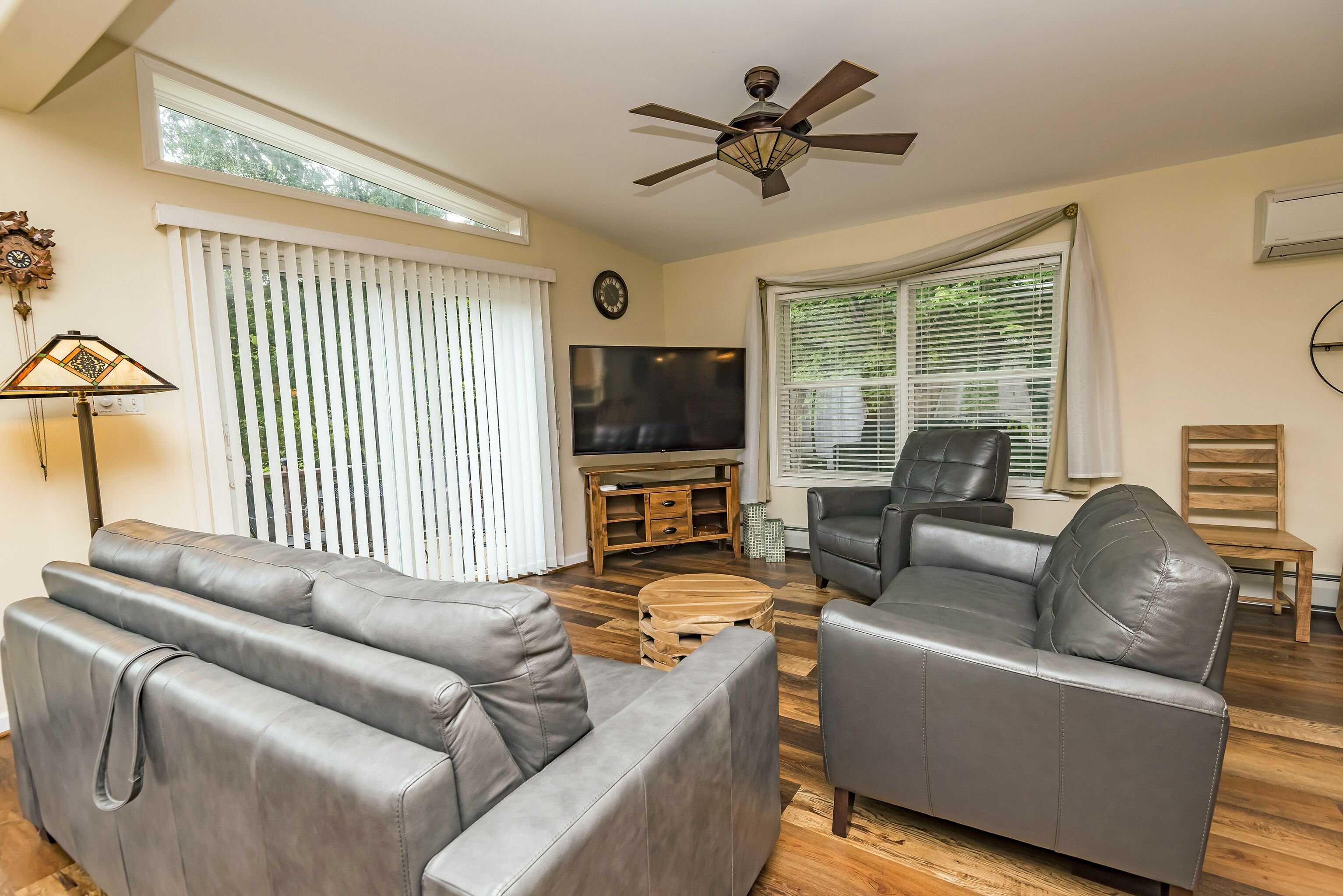 A living room with a grey leather sofa, a wooden coffee table, a TV, and a ceiling fan.