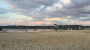 Ein Strand mit einem Rettungsturm, sandigem Ufer und ruhigem Wasser.