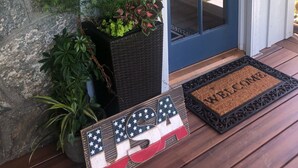 Un porche en bois avec un paillasson, une plante en pot et un drapeau américain en guise de décoration.