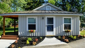 Une petite maison de plain-pied, dotée d’un toit à pignon, d’un porche à l’avant et d’une porte d’entrée.