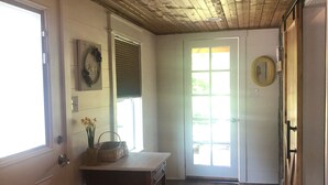 Un couloir avec un plafond en bois, une porte avec une fenêtre, une table avec un panier et des fleurs, et un tapis.