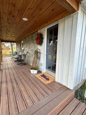 Een overdekt terras met houten vloer, een stenen muur, een deur met ruitpaneel en tuinmeubels met stoelen en een tafel.