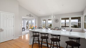 A kitchen with a white island, black bar stools, and large windows with a view.