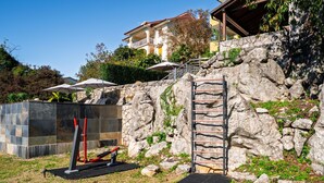 A stone wall with a metal ladder, outdoor exercise equipment, and a paved area.