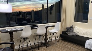 Un soggiorno moderno con un'ampia finestra, una zona pranzo con tavolo e sedie, e un divano con una soffice coperta bianca.