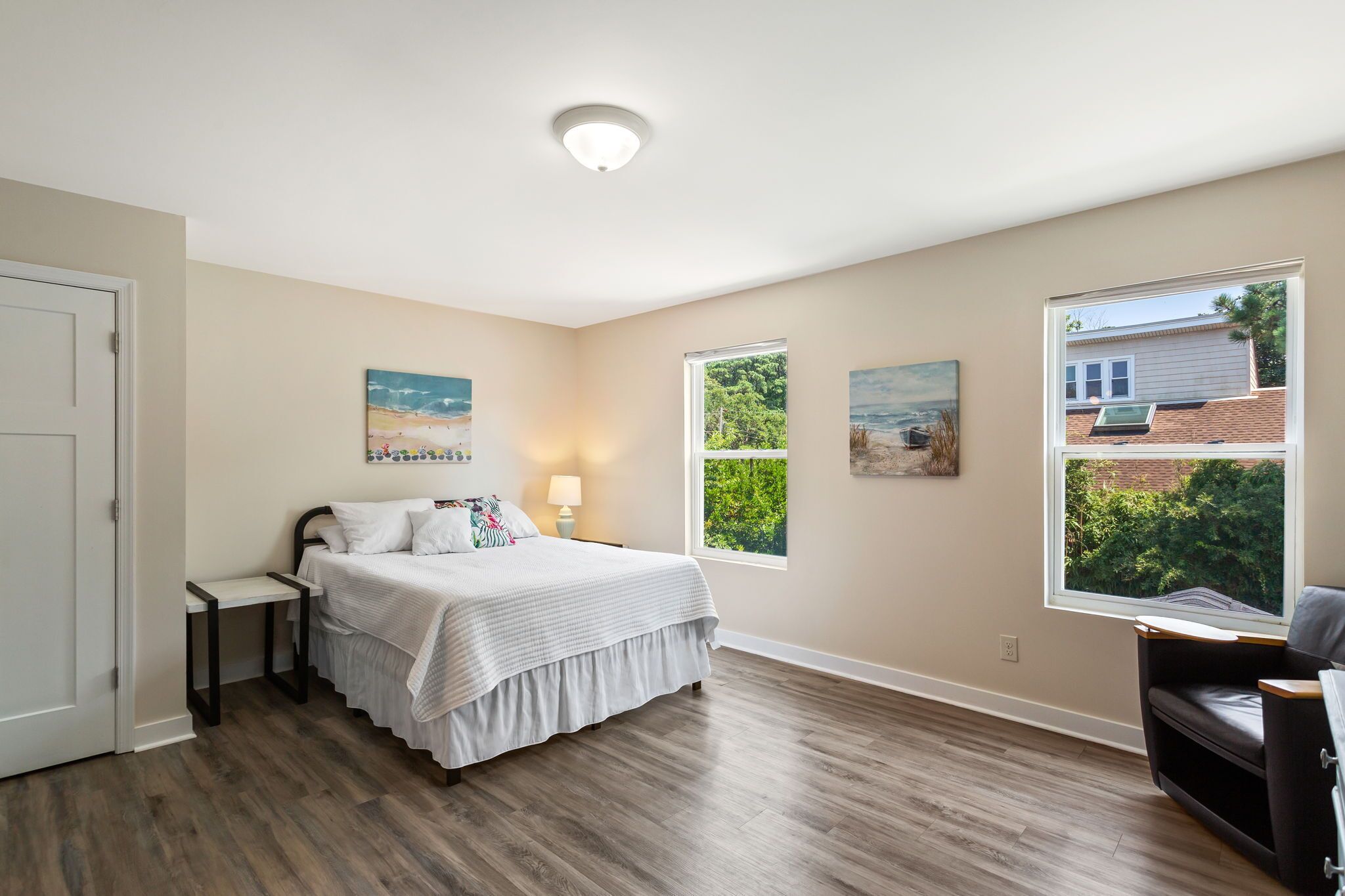 A bedroom with a bed, bedside tables, a chair, and two windows.