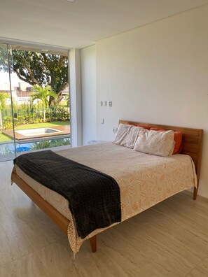 Relax in a serene bedroom with a large bed, geometric patterned bedspread, and a balcony offering a garden view.