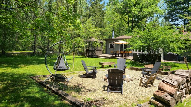 Ein Garten mit Schaukel, Adirondack-Stühlen, Grill und einem kleinen Holzhaus.