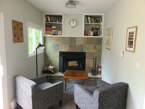 A living room with two grey upholstered chairs, a wooden coffee table, a fireplace, and bookshelves filled with books. - Family Getaway w/ year round  Hot Tub
 (Three Oaks)