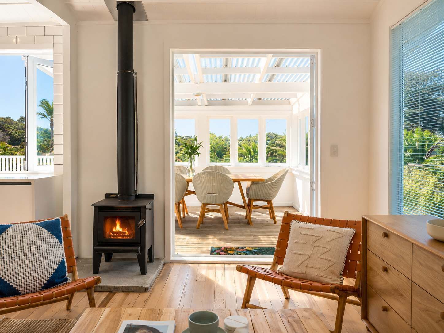 Une pièce chaleureuse avec une cheminée, des meubles en osier et une vue sur un patio aménagé avec des sièges d’extérieur.