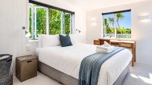 A modern bedroom with a large bed, two windows, a desk, and a trash bin. - Bluebelle - Huruhi Bay Sea Views (Waiheke Island)