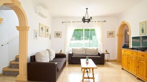 Un soggiorno con divano, tavolo e mobile TV. Si vedono delle scale che portano a un balcone.