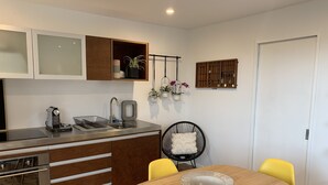 Een moderne keuken met een inbouwoven, een spoelbak en een eethoek met een houten tafel en twee gele stoelen.