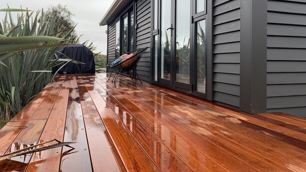 Een houten terras met een overdekte barbecue en een lounge stoel.