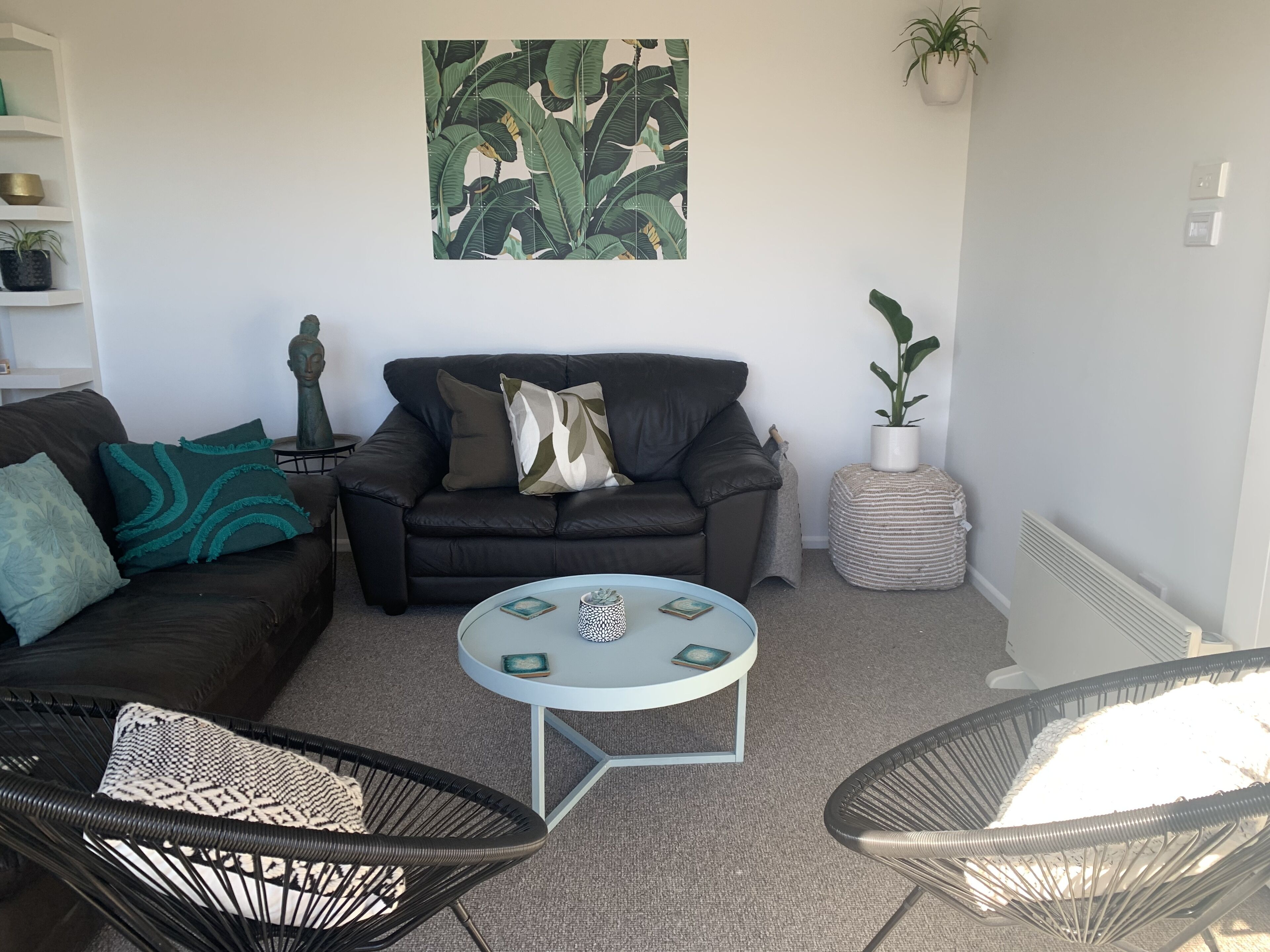 A living room with a black leather sofa, two black wicker chairs, a small round table, and a potted plant.