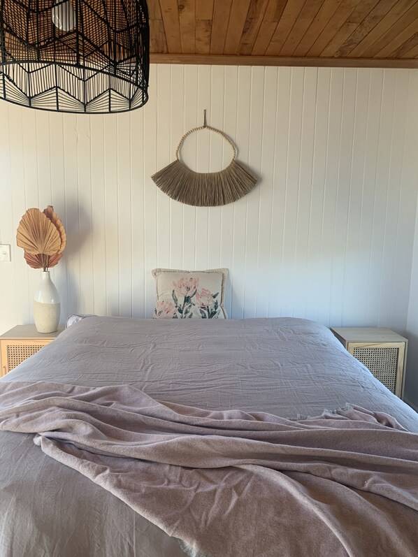 A bedroom with a bed, a wall-mounted macrame piece, a decorative vase, and a woven hanging light fixture.