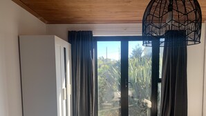 Een slaapkamer met een grote schuifdeur naar een tuin, een bed en een hanglamp.