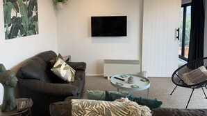 Een moderne woonkamer met een bank, een ronde salontafel, een televisie en een schuifdeur naar een buitenruimte.