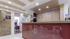 A reception area with a marble counter, a wooden wall with the hotel name, and a visible door leading to a dining area. - Hotel Florencia Plaza (Medellín)