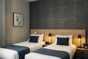 Una camera d'albergo con due letti, un muro in pietra e un quadro appeso.