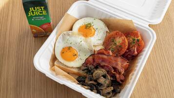 A meal in a takeout container with eggs, bacon, tomatoes, mushrooms, and toast.