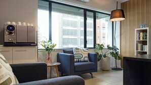 A modern living room with a coffee machine, a sofa, a side table, and a bookshelf. - Quest 256 Lambton (Wellington)