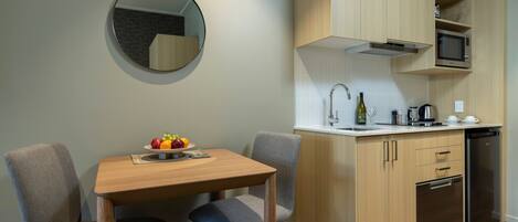 Una cocina compacta con armarios de madera, microondas, pileta y comedor con mesa y dos sillas.