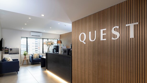 A modern hotel lobby with a reception desk, a seating area with sofas, and a large 'QUEST' sign on the wall. - Quest 256 Lambton (Wellington)