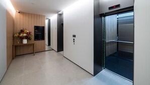 A modern hallway with an elevator, a reception desk with a floral arrangement, and a digital display. - Quest 256 Lambton (Wellington)