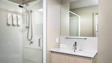 Un baño moderno con cabina de ducha de vidrio, un lavabo blanco y un espejo grande.
