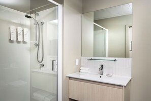 A modern bathroom with a glass shower enclosure, a white sink, and a large mirror. - Quest 256 Lambton (Wellington)