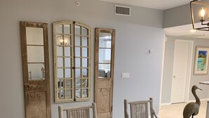 Zona pranzo con tavolo in vetro, sedie bianche con cuscini a motivi blu e specchi con cornice in legno.