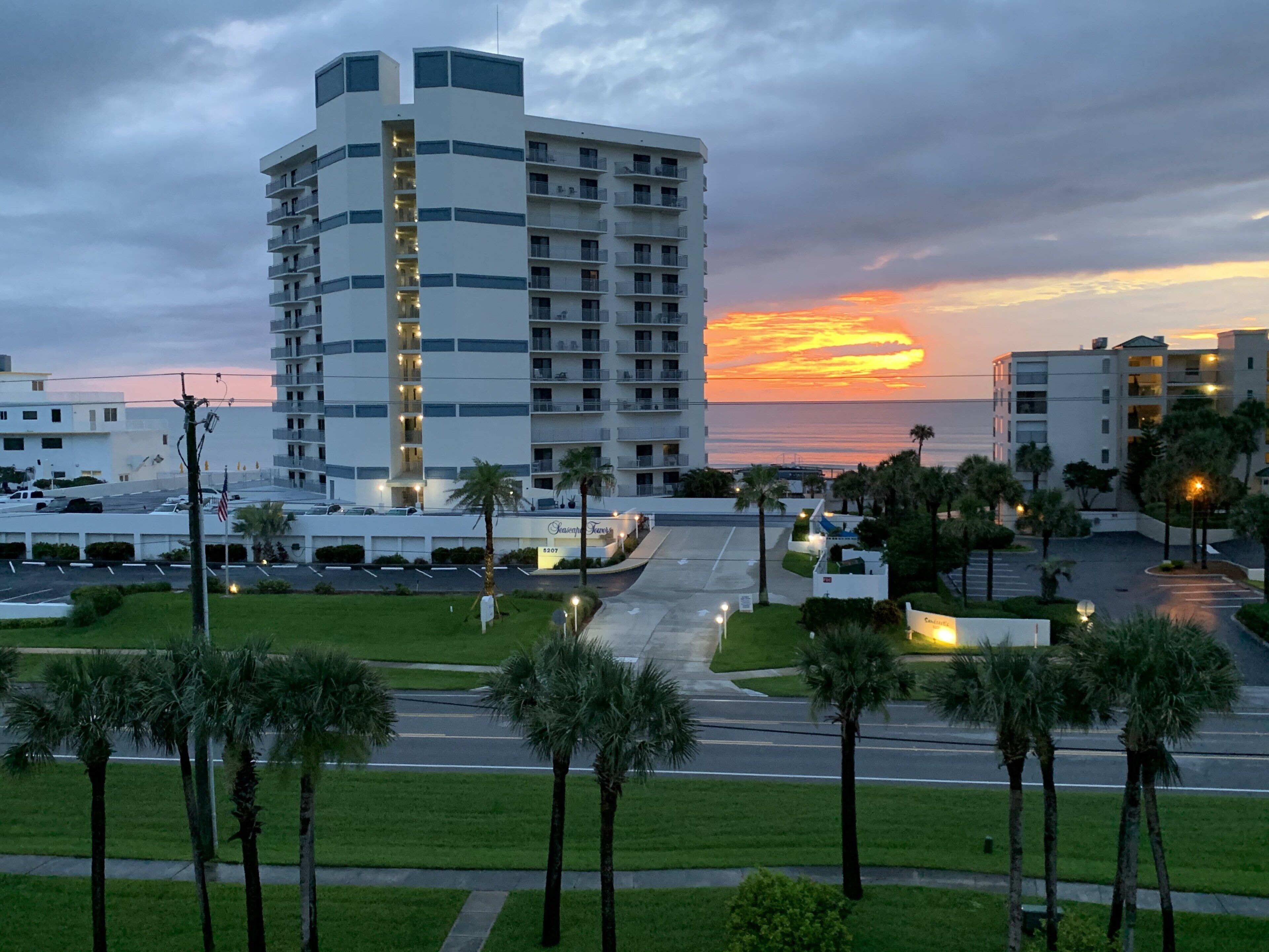 A multi-story hotel with a central atrium, a parking lot, and palm trees in the foreground.