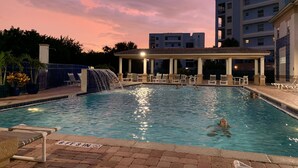 Una piscina con cascata, poltrone a sdraio e una zona relax coperta.
