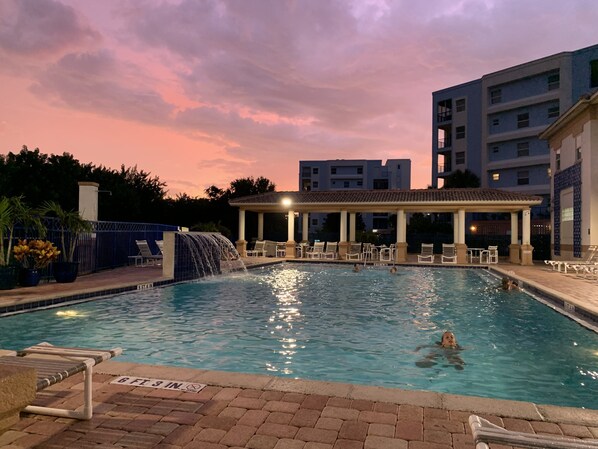 A swimming pool with a waterfall feature, lounge chairs, and a covered seating area.