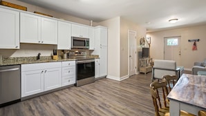 A modern kitchen with white cabinets, stainless steel appliances, and a granite countertop. - Adorable Chesapeake Bay Beach Cottage B Just 1 Block from the Sand! (Virginia Beach)