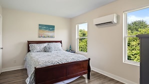 A bedroom with a wooden bed, a painting on the wall, and a window with a view of greenery. - Adorable Chesapeake Bay Beach Cottage B Just 1 Block from the Sand! (Virginia Beach)
