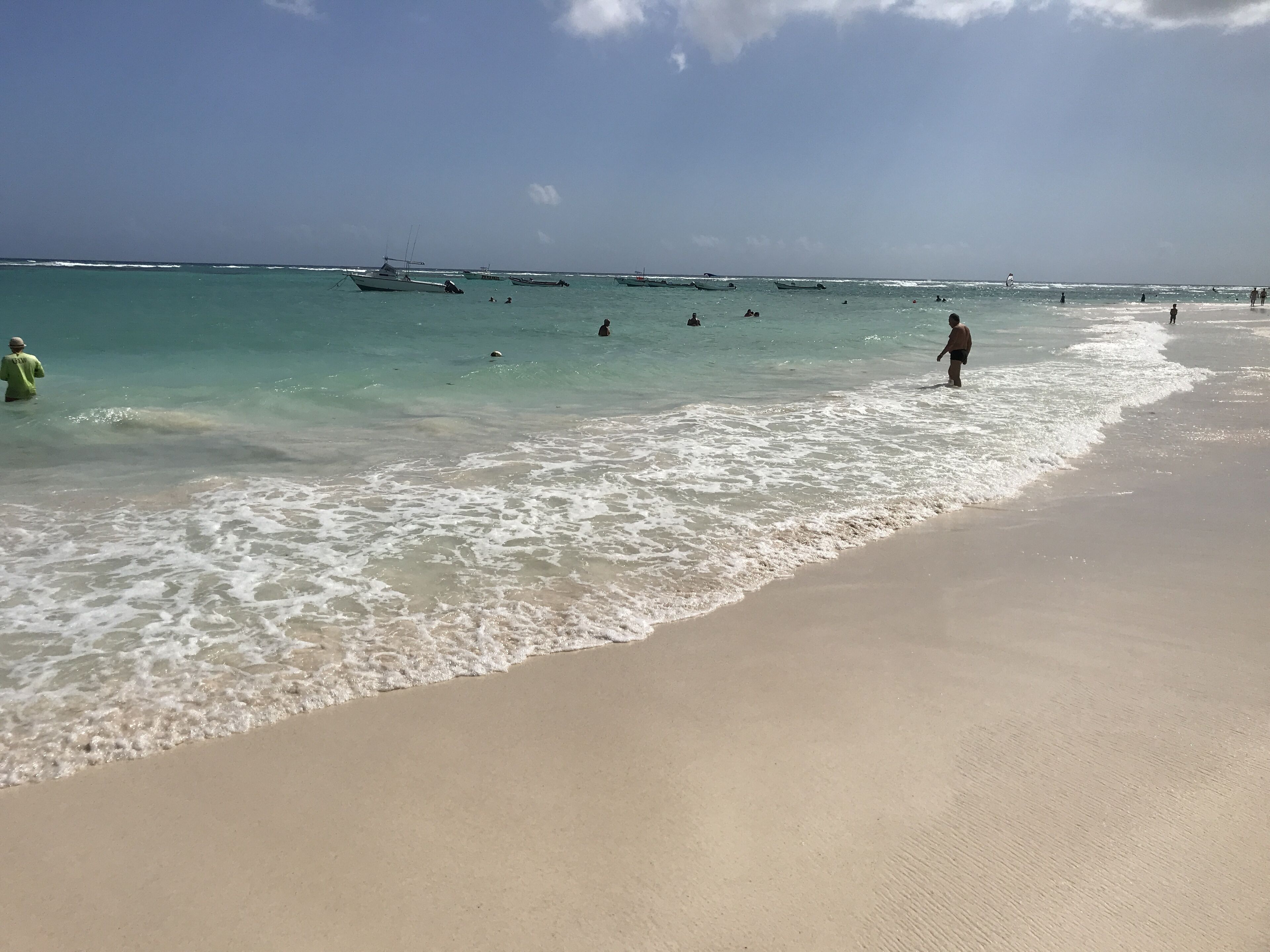 Een strand met helder water, boten en mensen.
