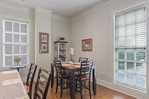 A dining area with a wooden table and chairs, framed artwork on the walls, and a window with blinds. - Bay St Beauty 2 Bedroom Condo in the Heart of SAV (Savannah)