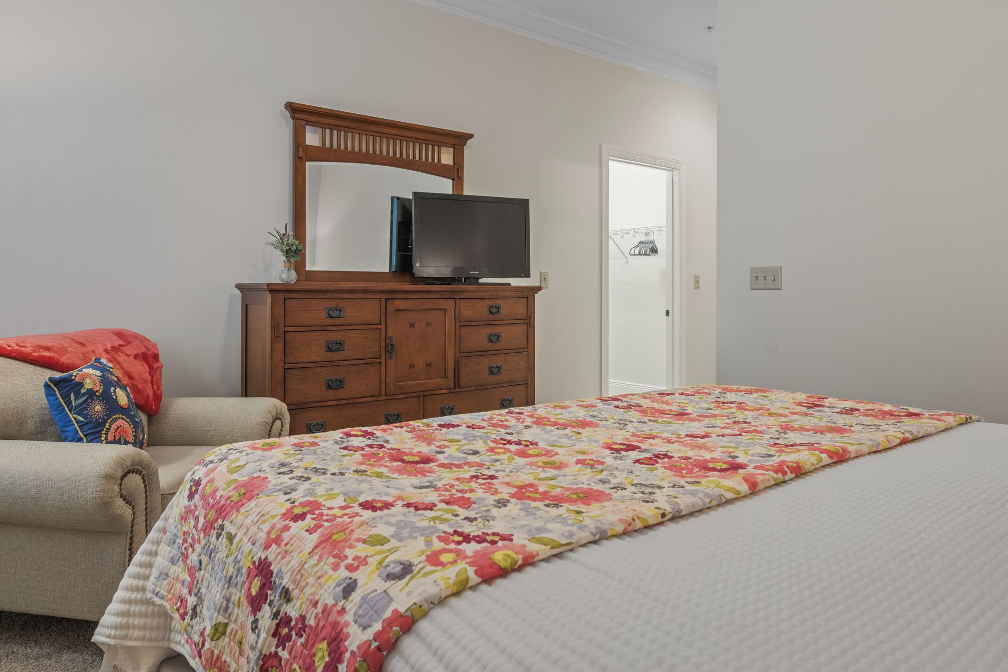 Une chambre à coucher avec un lit, une commode sur laquelle se trouve un téléviseur, et une porte.
