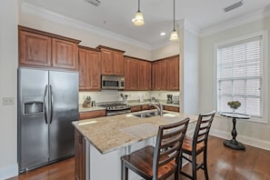 A modern kitchen with wooden cabinets, stainless steel appliances, granite countertops, and a dining area with a table and chairs.