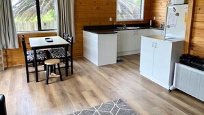 A compact kitchen with a dining area, wooden walls, and a view of greenery outside.