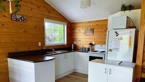 A compact kitchen with wooden walls, a window, white cabinets, and a refrigerator.