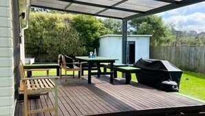 A covered patio with a table and chairs, a barbecue grill, and a small shed.