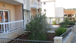 Un immeuble résidentiel doté de balcons, d’un petit jardin et d’un mur en pierre.