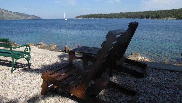 Une chaise en bois et un banc au bord d’un lac, avec un voilier visible au loin.